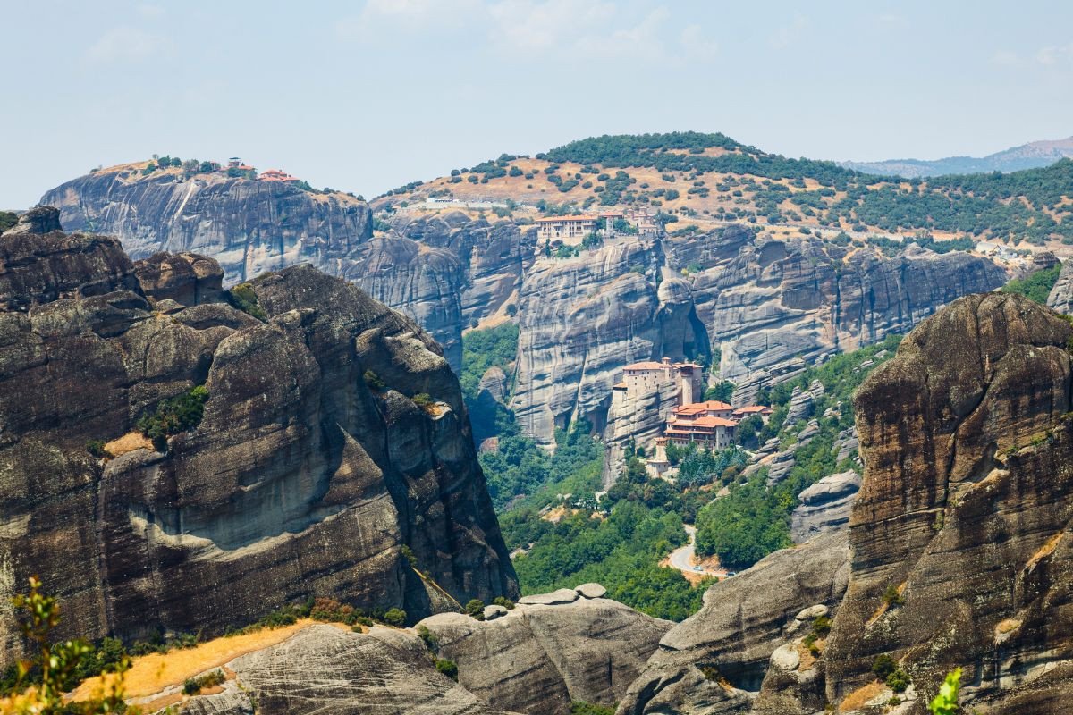 Monasteries perched on top of tall rock formations in Meteora, Greece, surrounded by rugged cliffs and sparse vegetation.